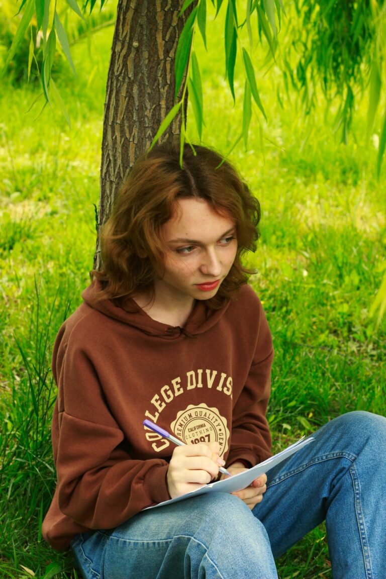Adolescente en sweat qui écrit sous un arbre en été